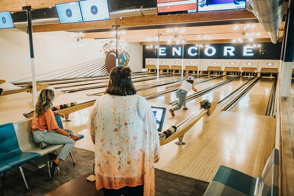 A woman rolling a bowling ball while two friends watch