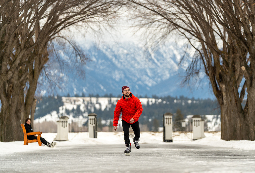 A Man in a Red Jacket skating outside while another person watches from the bench