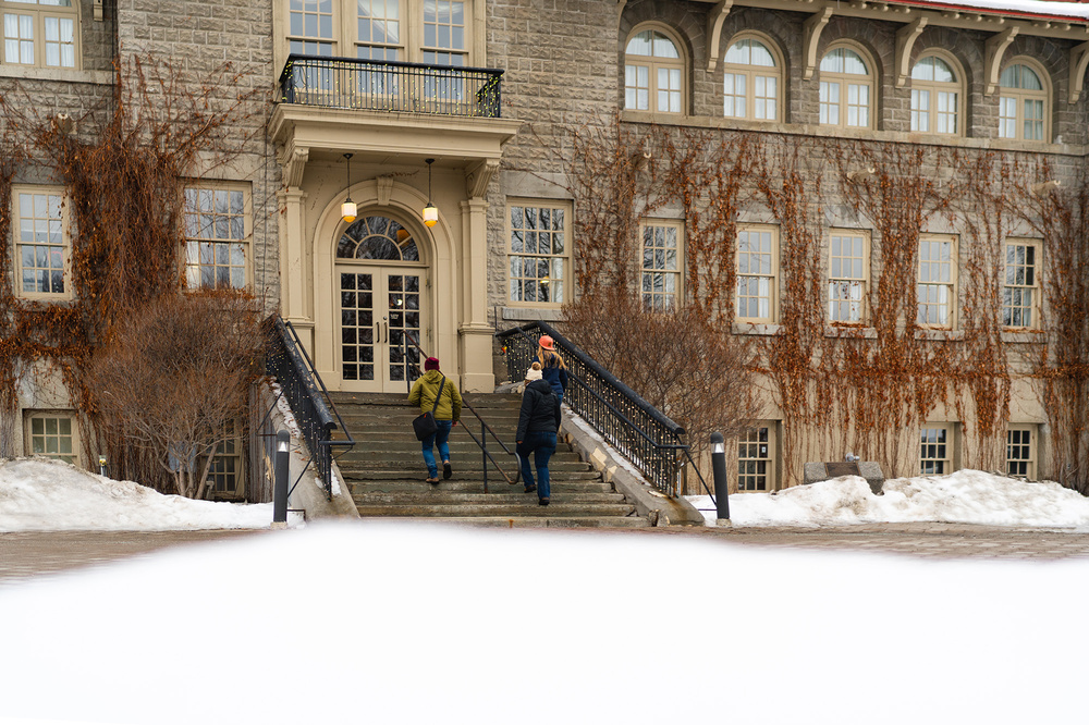 Three people walking up stairs to an entrance to a building covered in ivy